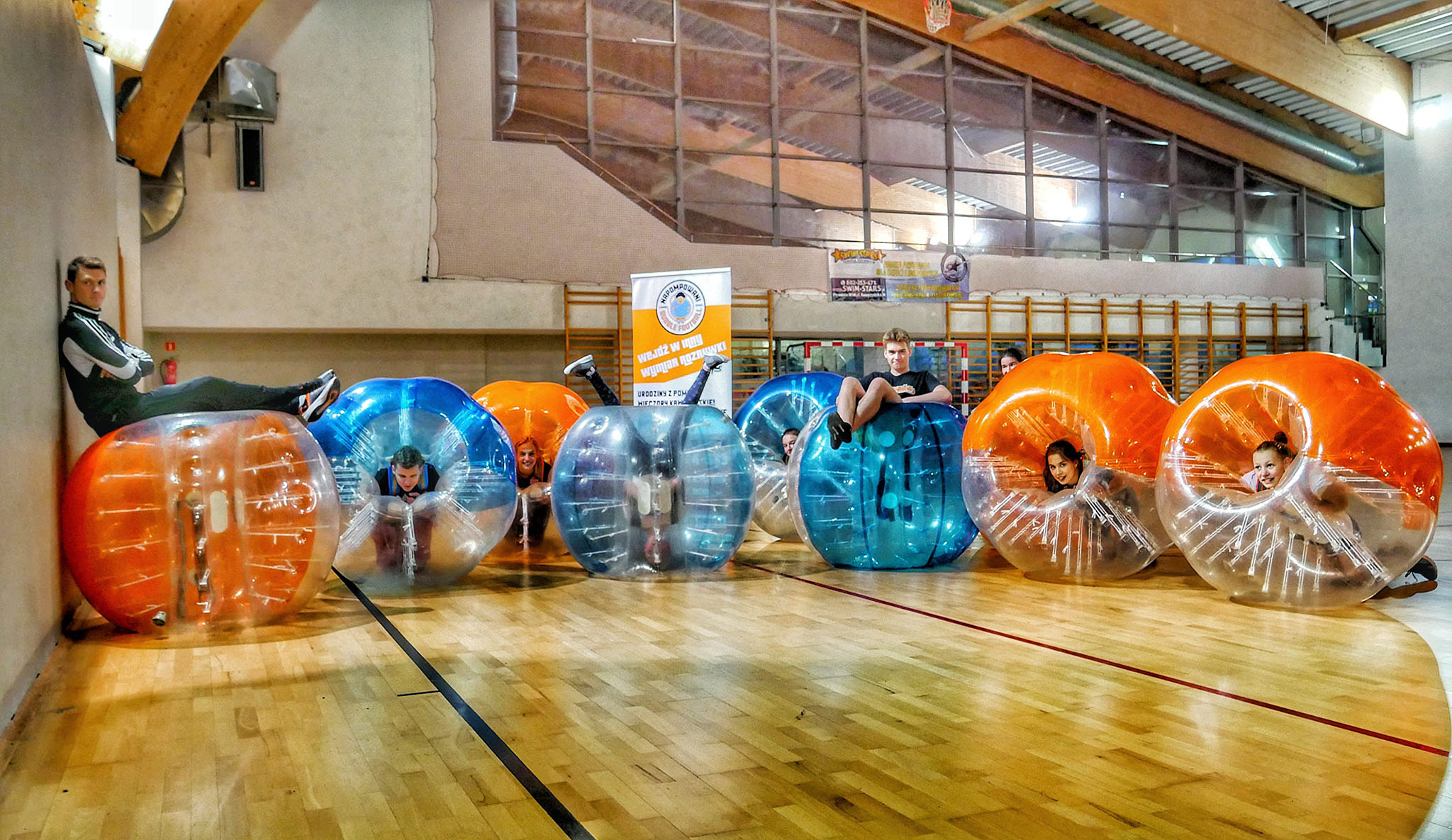 Dzieci w pomarańczowych i niebieskich kulach Bubble Football z trenerem
